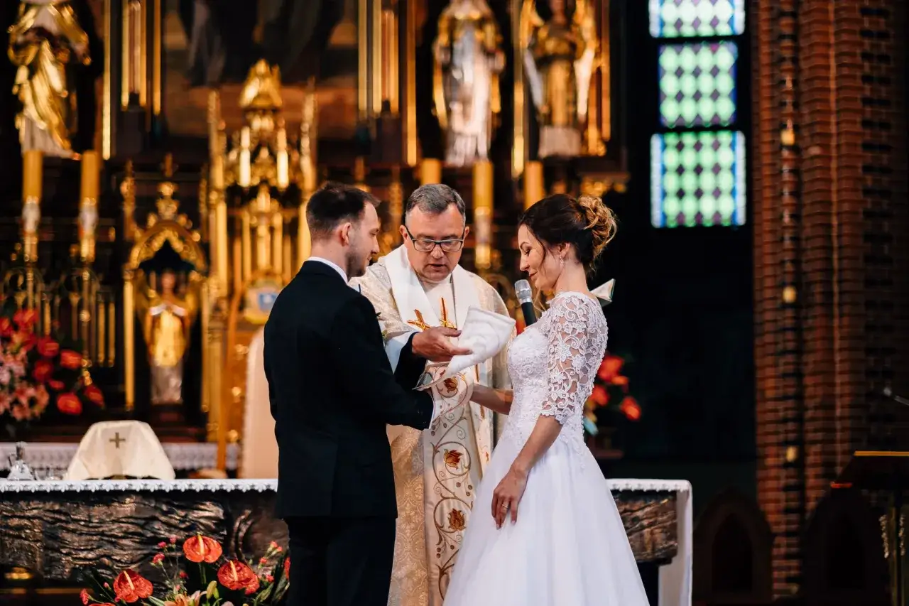 Para spowiedzi przedślubnej lub formalności w USC: narzeczeni słuchają księdza w kościele, przygotowując się do sakramentu małżeństwa.