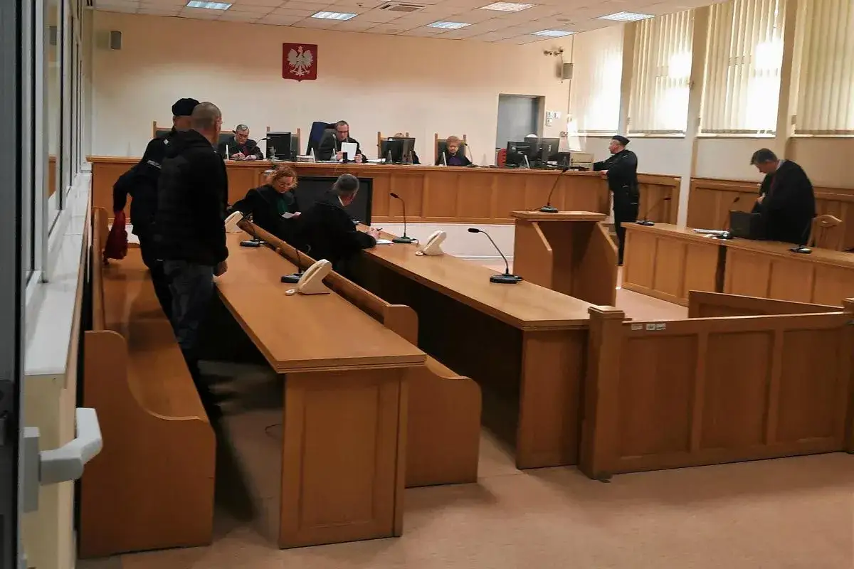 W sali sądowej, gdzie panuje napięcie, widać ławę przysięgłych, czyli **list żelazny** w przenośni. Sędziowie i uczestnicy procesu siedzą przy drewnianych stołach.