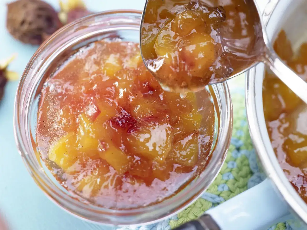 Ein Löffel voller glänzender Nektarinen Marmelade wird über ein Glas voller Fruchtstücke geschöpft.