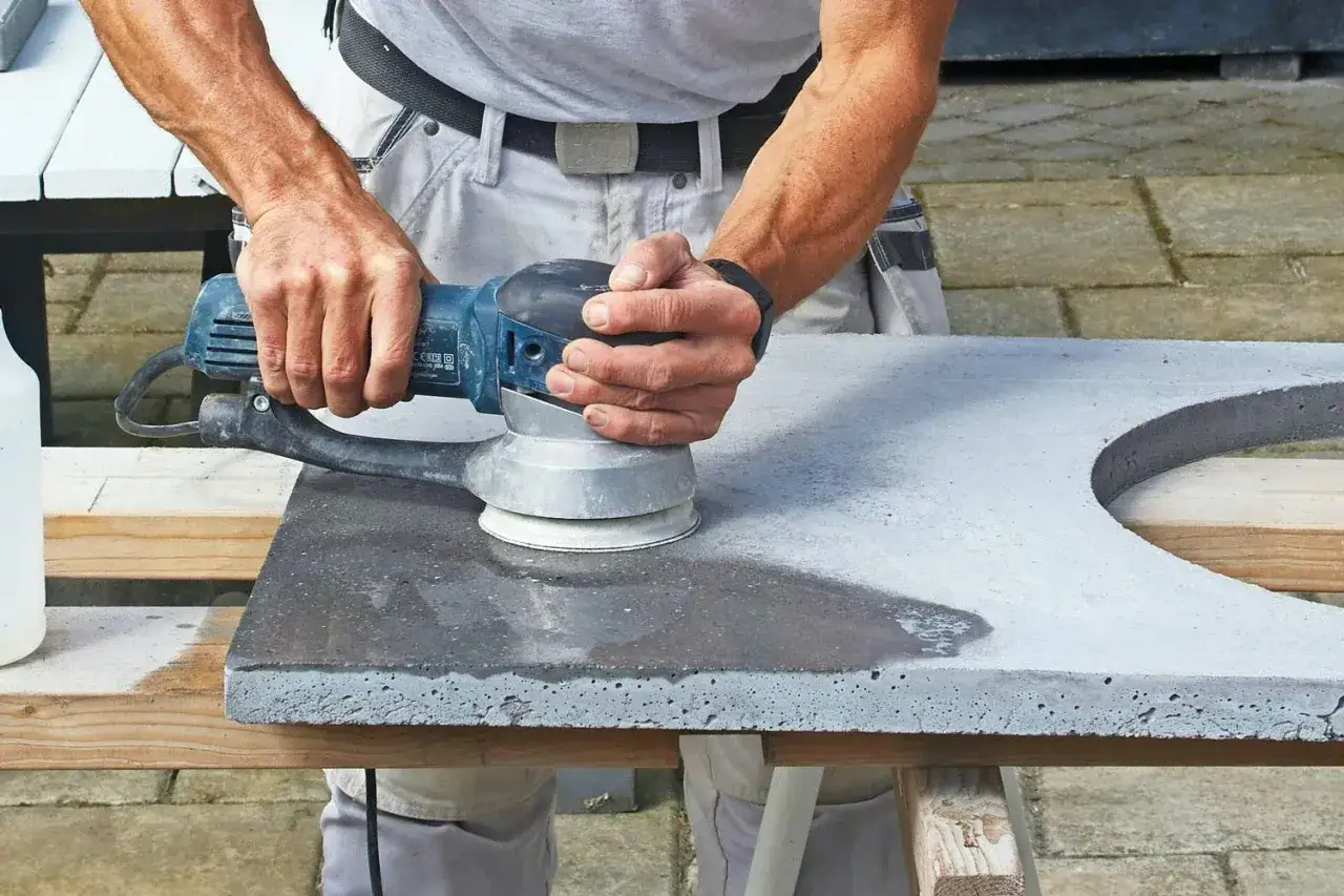 Händer slipar betonggolv med en maskin.