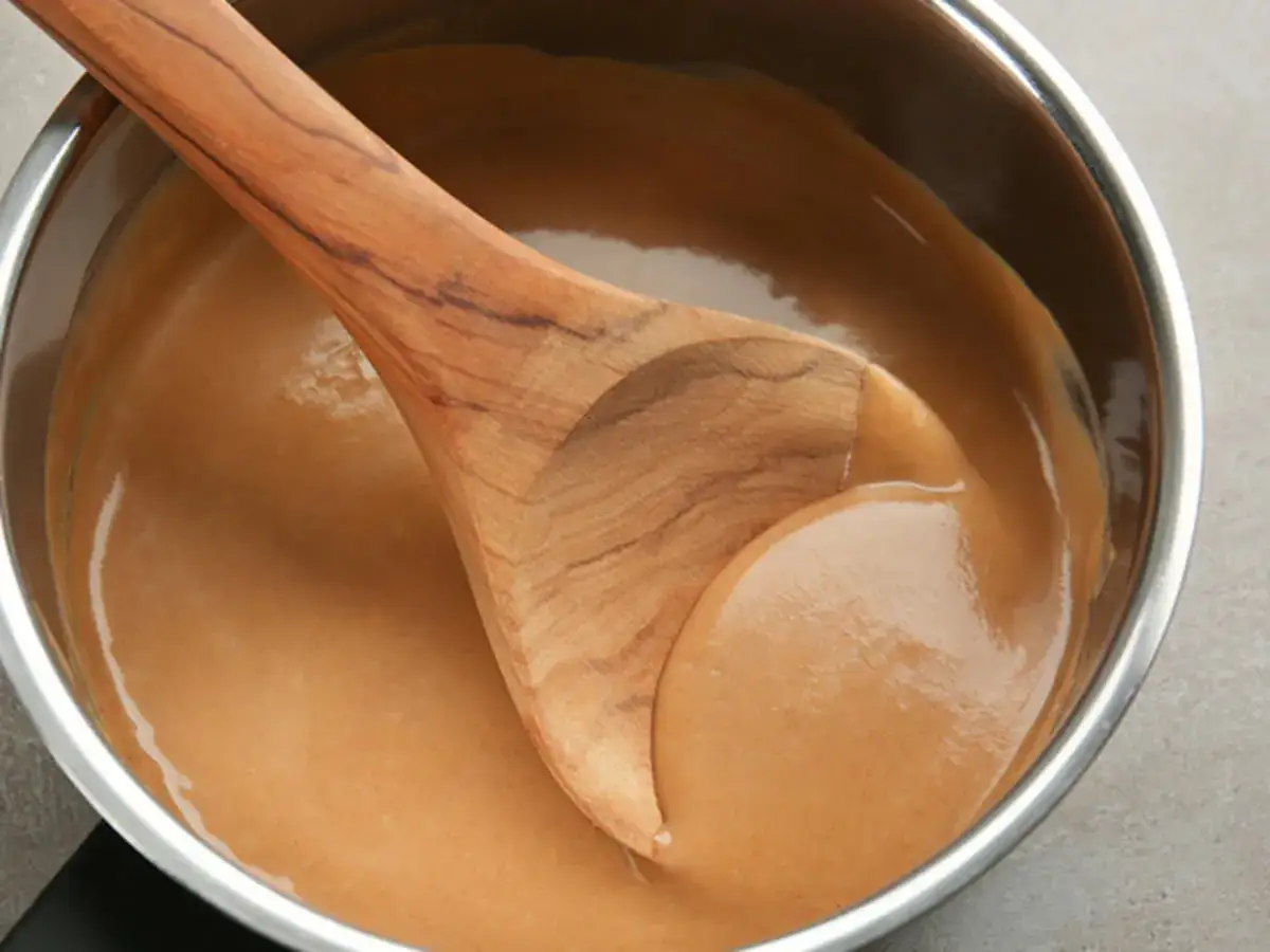 Holzkochlöffel rührt in einem Topf eine cremige Metaxa-Sauce.