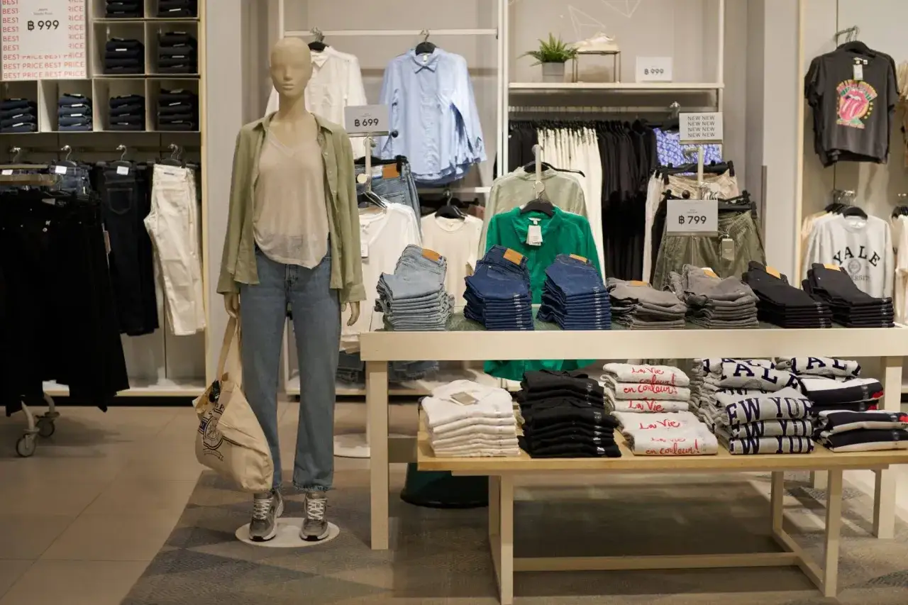 Skutki kupowania ubrań fast-fashion dla środowiska i portfela: stosy jeansów i koszulek w sklepie kuszą niskimi cenami, ale ich produkcja generuje odpady i zanieczyszczenia.
