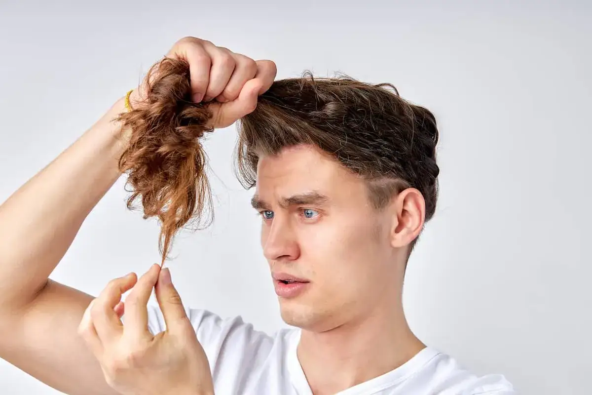 Mann mit blauen Augen prüft seine Haare, die trocken und gespalten aussehen. Was hilft gegen Spliss?