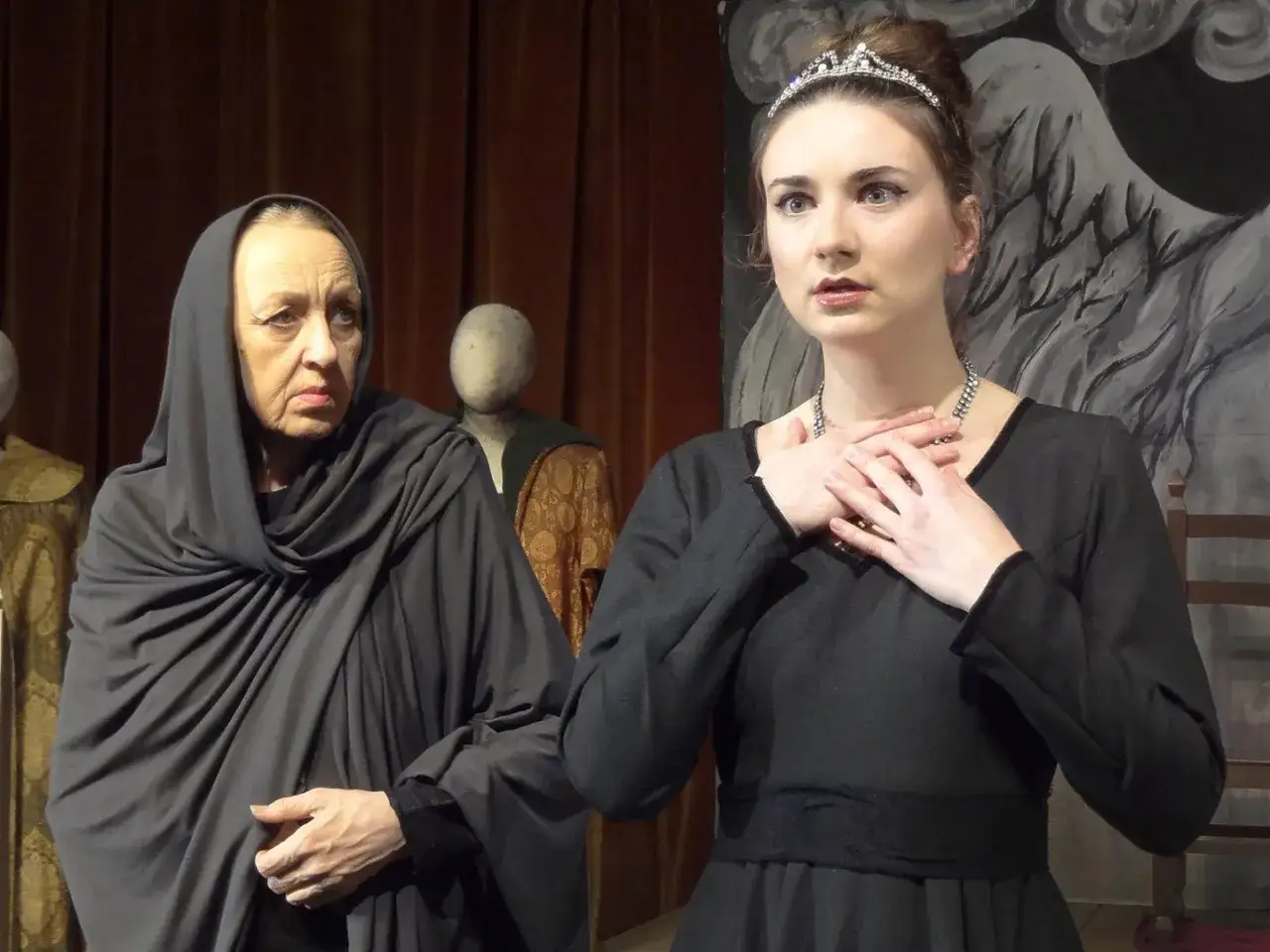 Dwie kobiety na scenie, jedna starsza w czarnym welonie, druga młoda w koronie. Scena z