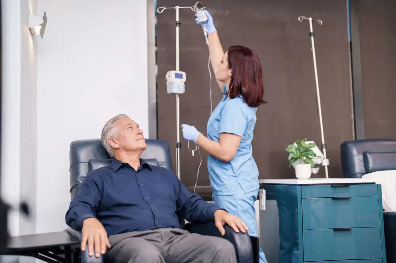 Un uomo anziano in poltrona riceve una flebo da un'infermiera. Questo &egrave; un esempio di terapia biologica cos'&egrave;.