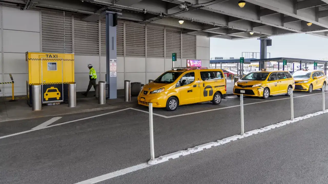 Gelbe Taxis in den USA warten auf Fahrgäste an einer Station. Ein Mann in Warnweste geht an einer gelben Taxihütte vorbei.