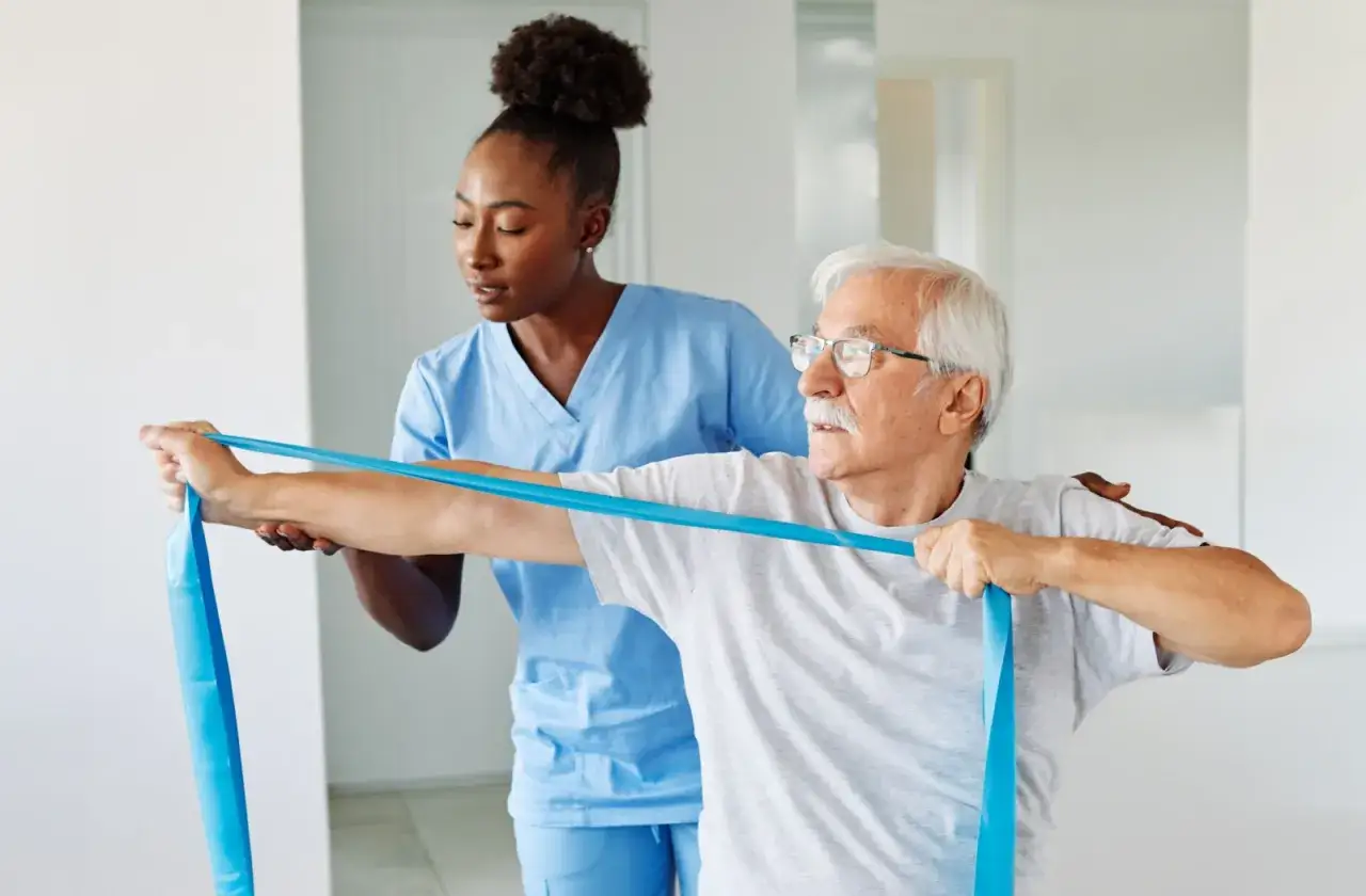 Fisioterapista assiste un anziano in esercizi con elastico, parte di un percorso di ginnastica per osteoporosi grave.