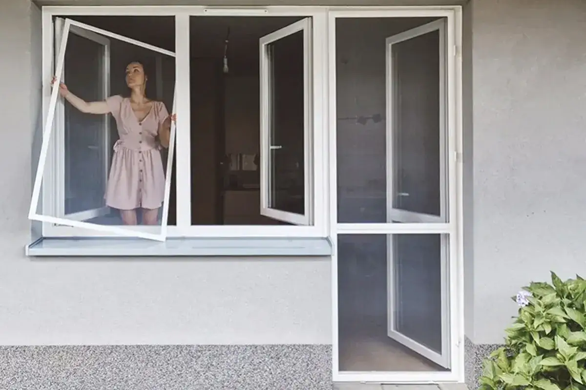 Kobieta montuje moskitierę na okno. Prosty spos&oacute;b, jak zamontować moskitierę na okno, by cieszyć się świeżym powietrzem bez owad&oacute;w.