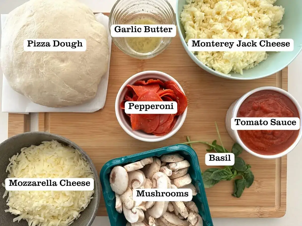 Składniki na najlepsza pizza przepis: ciasto, sos pomidorowy, ser mozzarella, pieczarki, pepperoni, masło czosnkowe, bazylia i ser Monterey Jack.