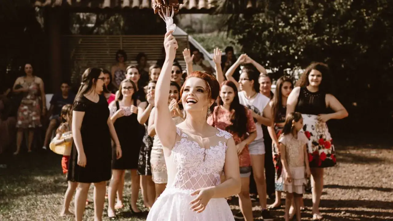 Novia sonriente lanza el ramo de novia a un grupo de mujeres expectantes.