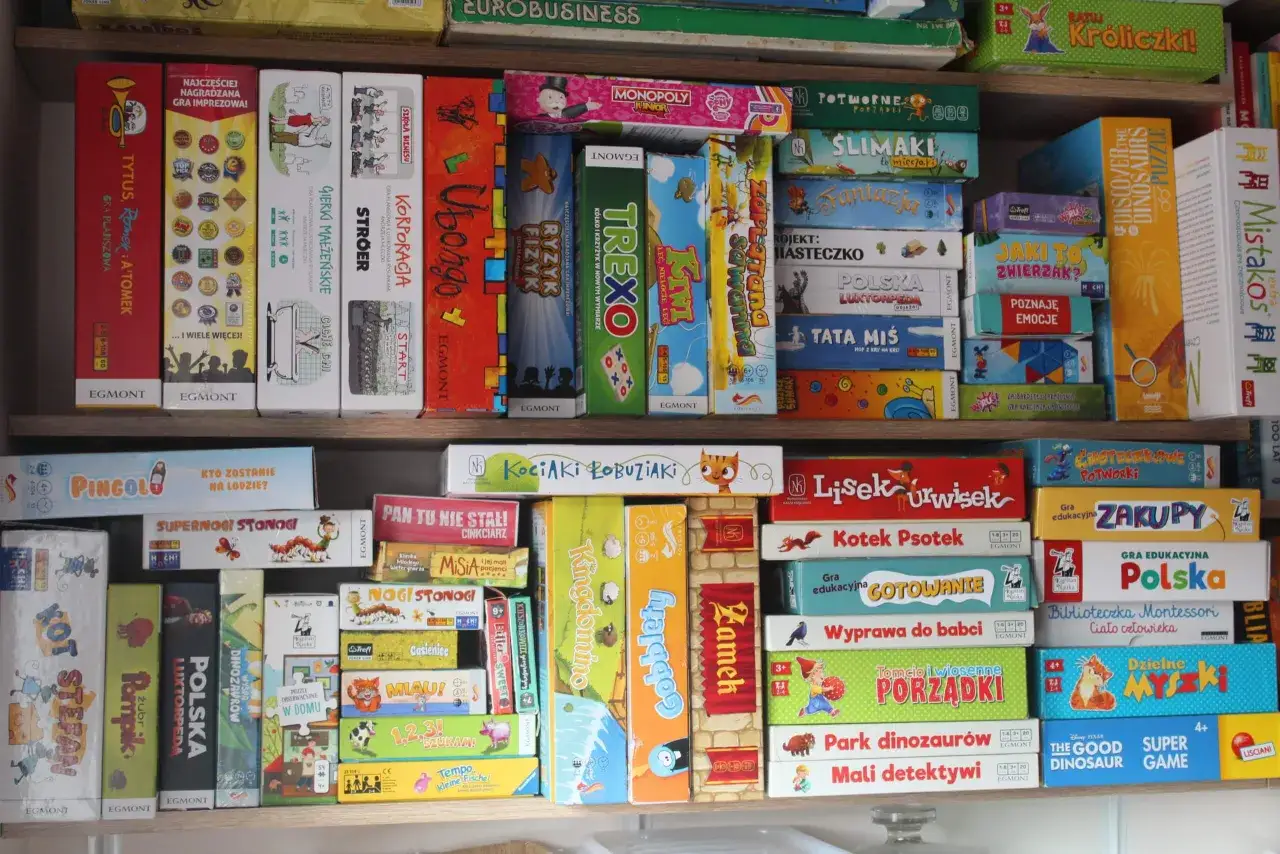 Półki pełne gier planszowych, od szybkich gier imprezowych po edukacyjne, dla dzieci i dorosłych.