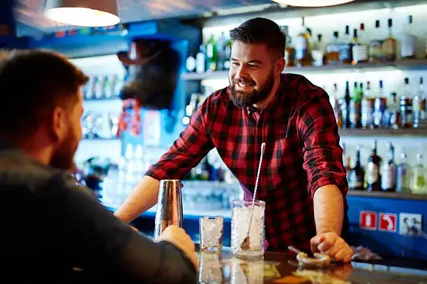 barman rozmawiający z uśmiechniętym gościem przy barze