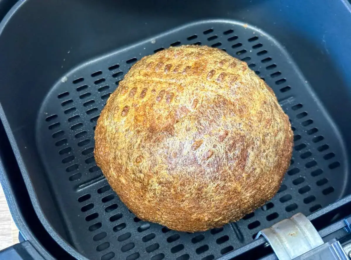 Ein goldbraunes Brot liegt in einem Airfryer. Das Ergebnis von **Brot backen im Airfryer** ist perfekt.