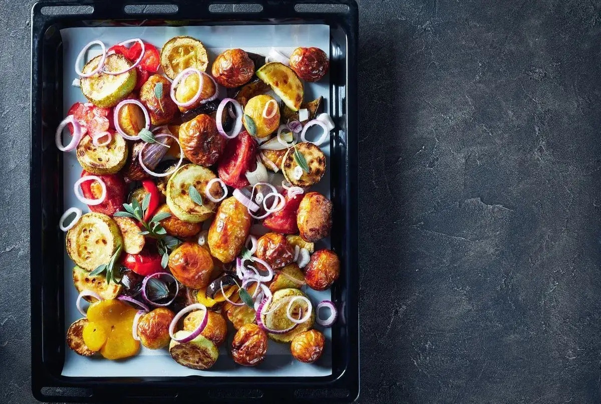 Un plateau de gratin de l&eacute;gumes color&eacute; et r&ocirc;ti, avec des rondelles d'oignon rouge et des herbes fra&icirc;ches.