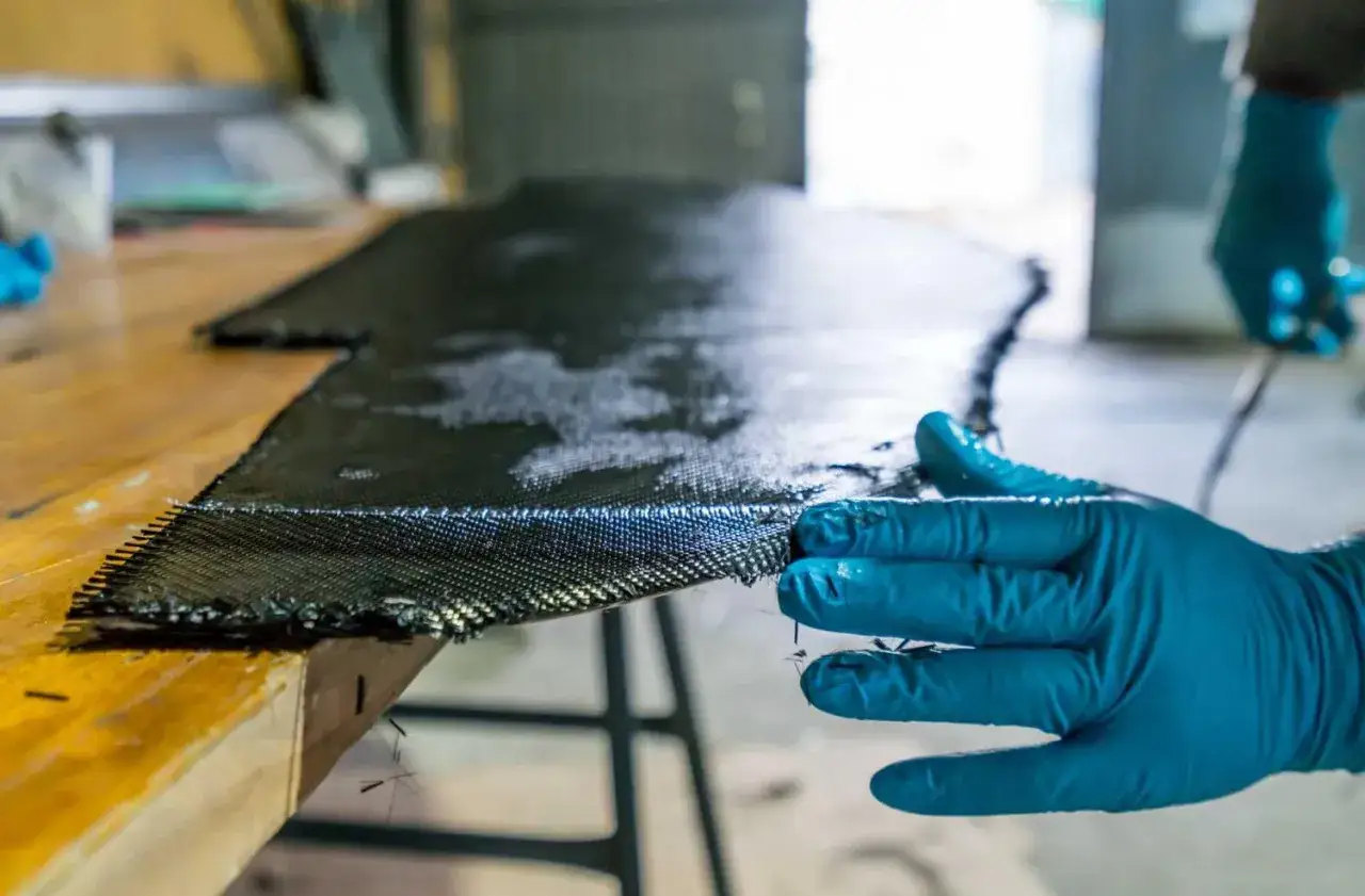 Hand in blauer Handschuh bearbeitet Carbonfaser-Gewebe für den epoxidharz bootsbau.