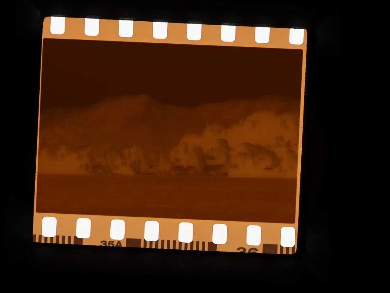 A vintage 35mm film strip shows a sepia-toned landscape of mountains, trees, and water. The film's perforations and numbering are visible.