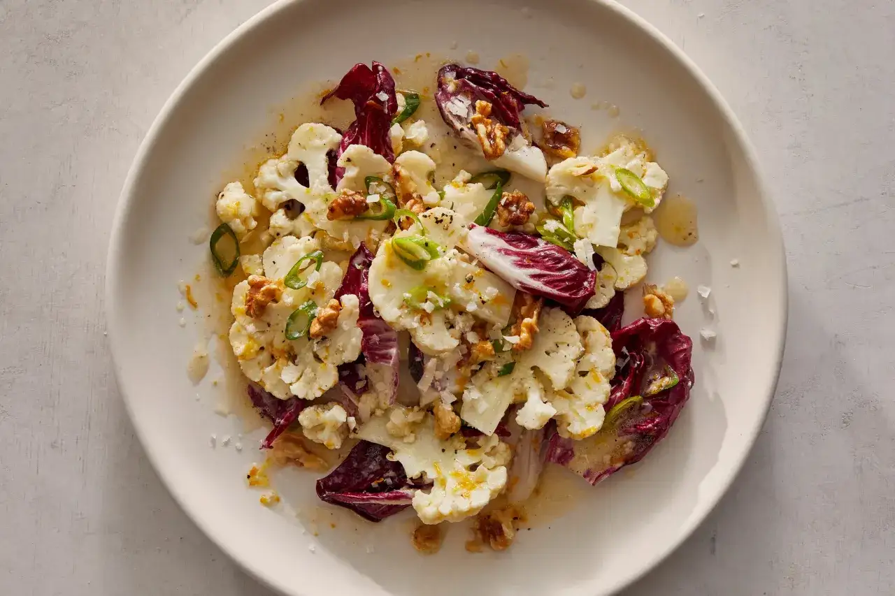 Orzeźwiająca sałatka z surowego kalafiora z radicchio, orzechami i zieloną cebulką, polana dressingiem.
