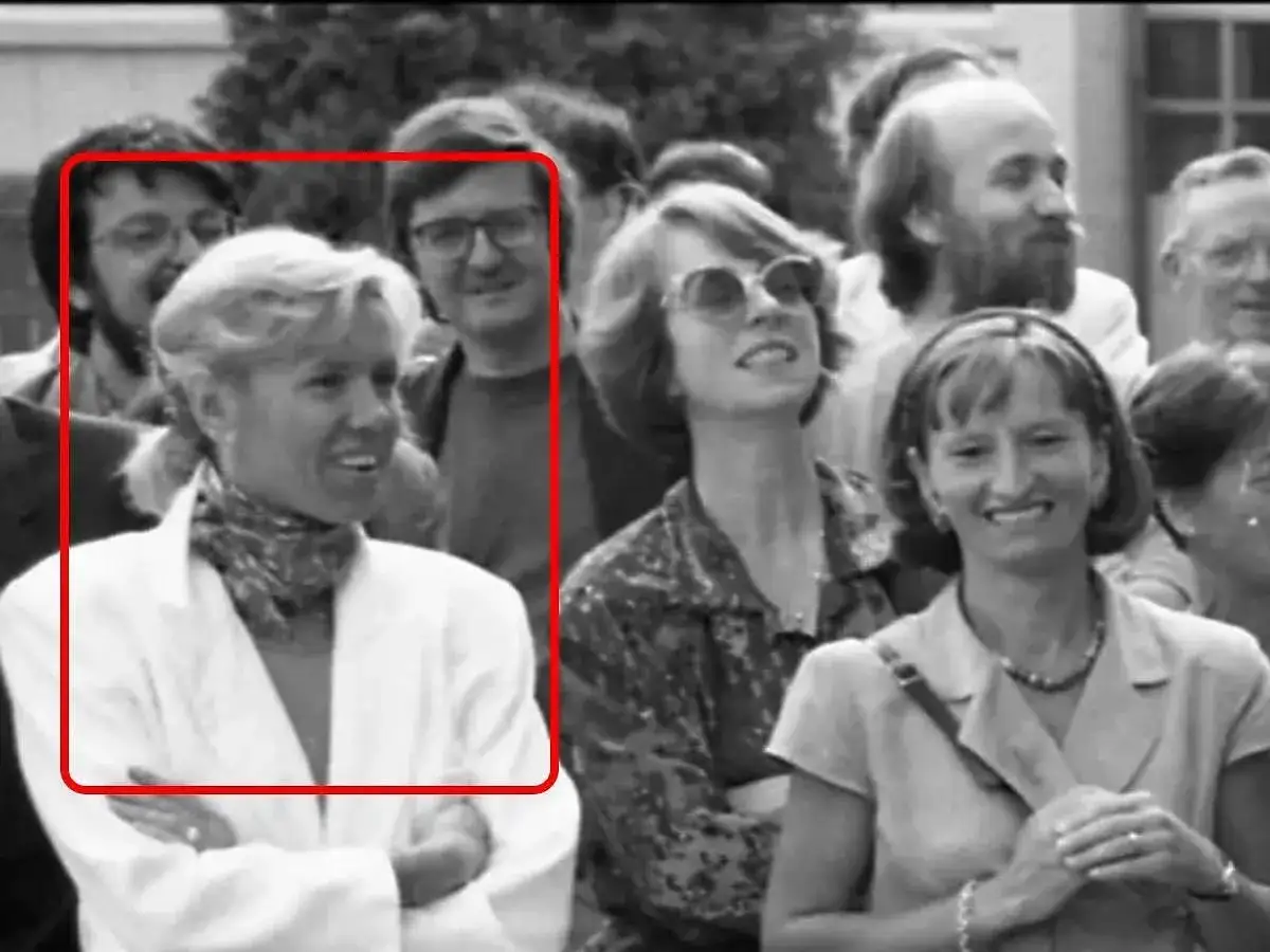 Brigitte Macron młoda, w białej marynarce i z apaszką na szyi, uśmiecha się do aparatu.
