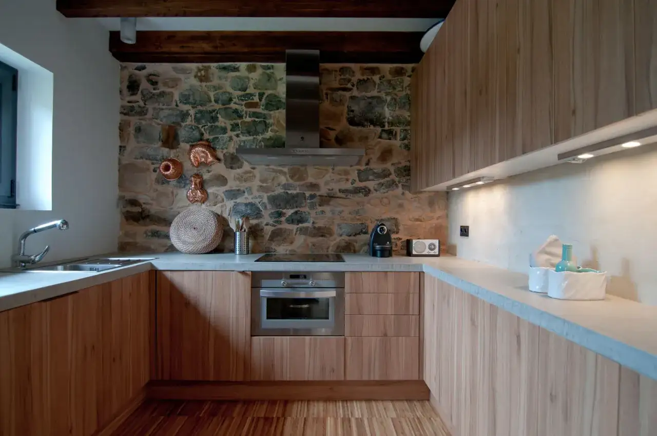Cocinas r&uacute;sticas modernas con pared de piedra, muebles de madera clara y encimera de hormig&oacute;n.