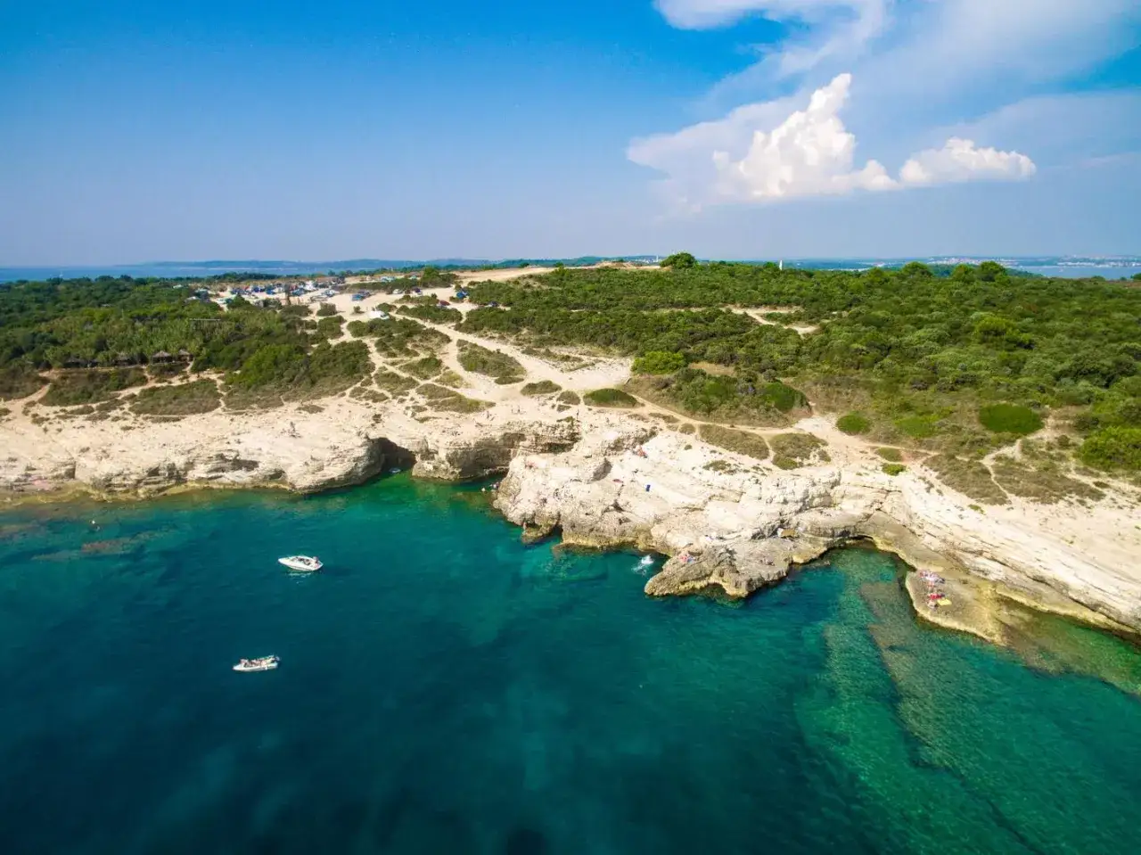 Luftaufnahme einer felsigen K&uuml;ste mit t&uuml;rkisfarbenem Wasser. Menschen genie&szlig;en die Sonne und das Meer, Boote ankern. Perfekte pula unternehmungen.