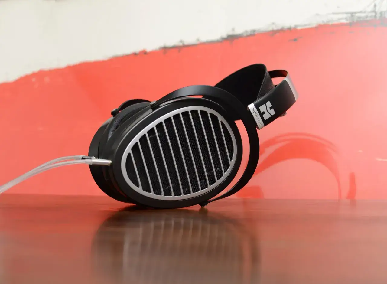Hifiman Ananda im Test: Hochwertige Kopfh&ouml;rer mit offenem Design auf einem Holztisch vor rotem Hintergrund.