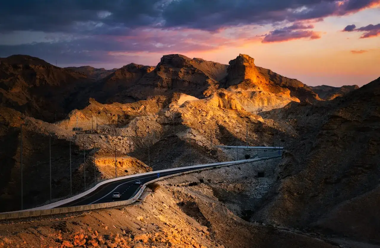 Droga wijąca się przez skaliste zbocza Jebel Hafeet w Al Ain, oświetlona złotym blaskiem zachodzącego słońca.