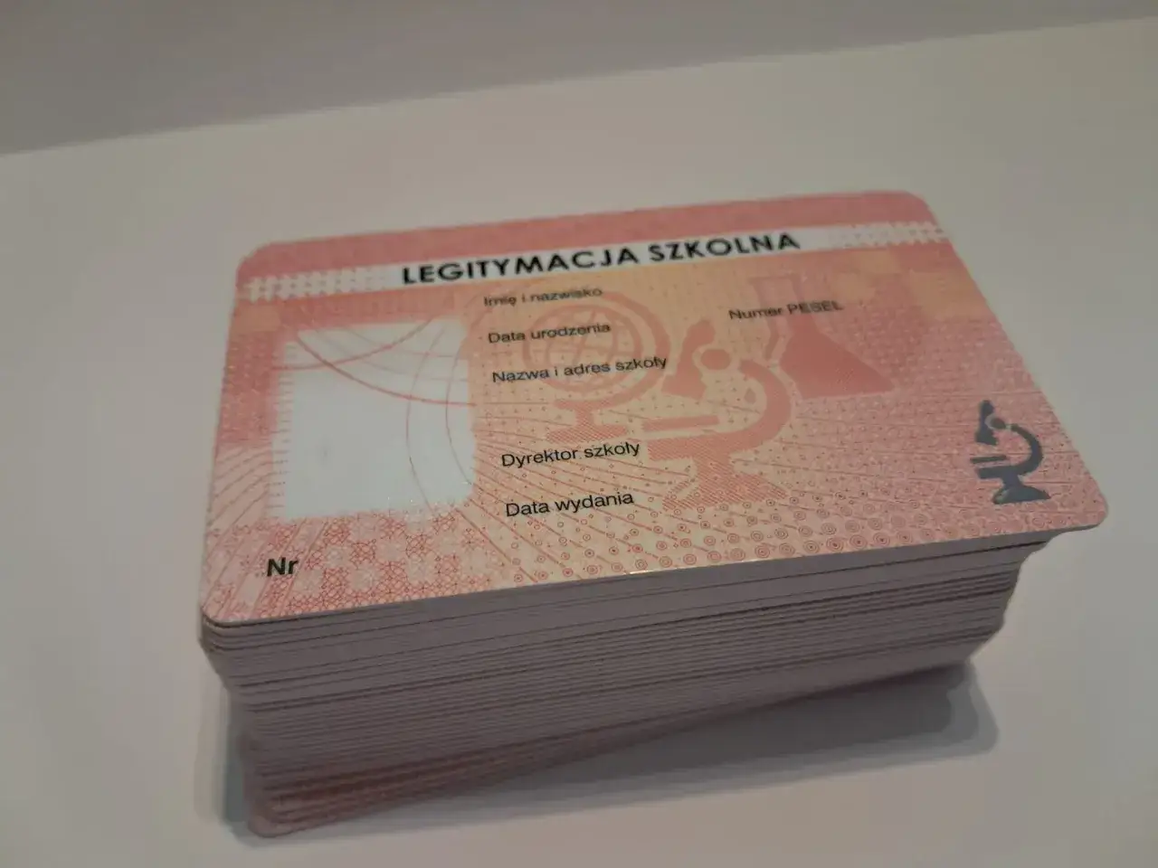 Stos nowych legitymacji szkolnych z mikroskopem i danymi ucznia.