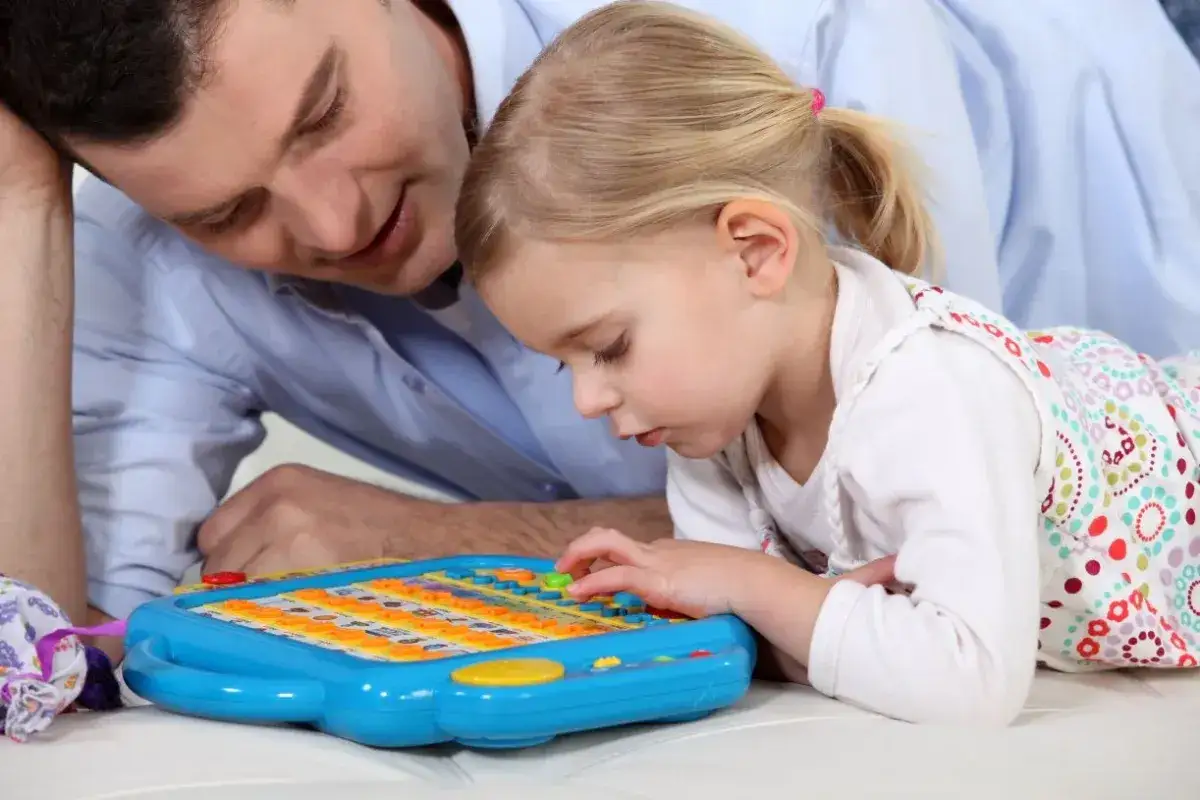 Ojciec z czułością obserwuje, jak jego córka bawi się zabawką edukacyjną. Widać, ile jest opieki na dziecko w tym wspólnym, spokojnym momencie.