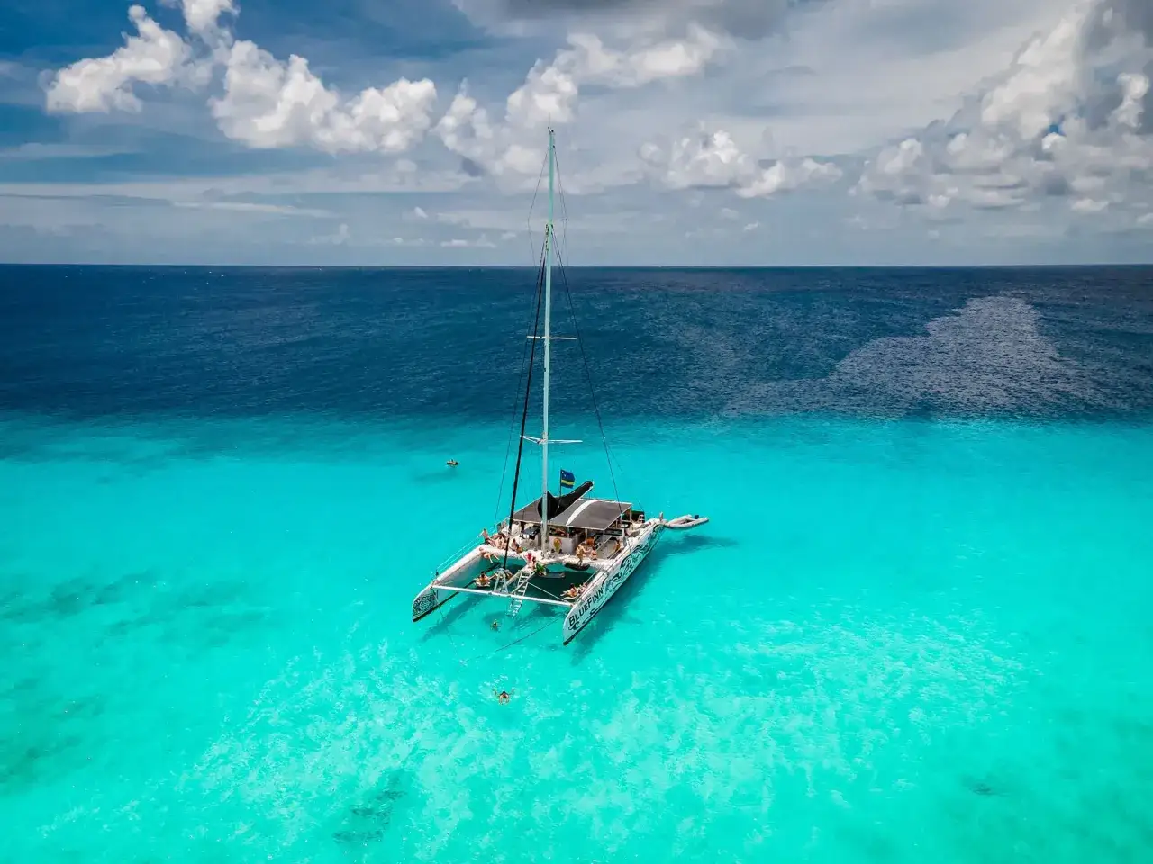 Ein Katamaran ankert im kristallklaren Wasser vor einem Curacao Beach. Menschen schwimmen und entspannen sich an Bord.