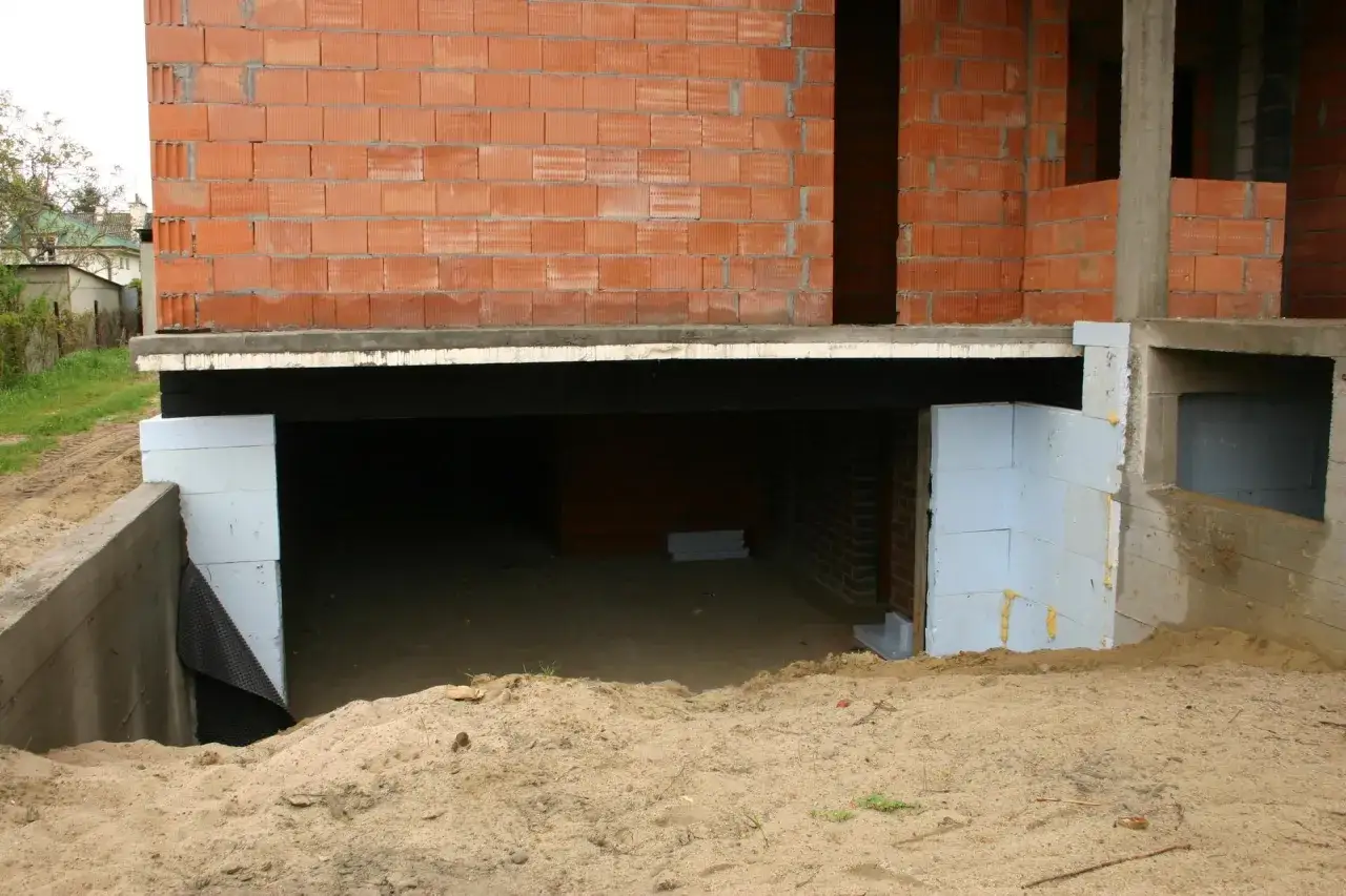 Budowa domu z piwnicą projekt: widok na fundamenty, ściany z pustaków i izolację.
