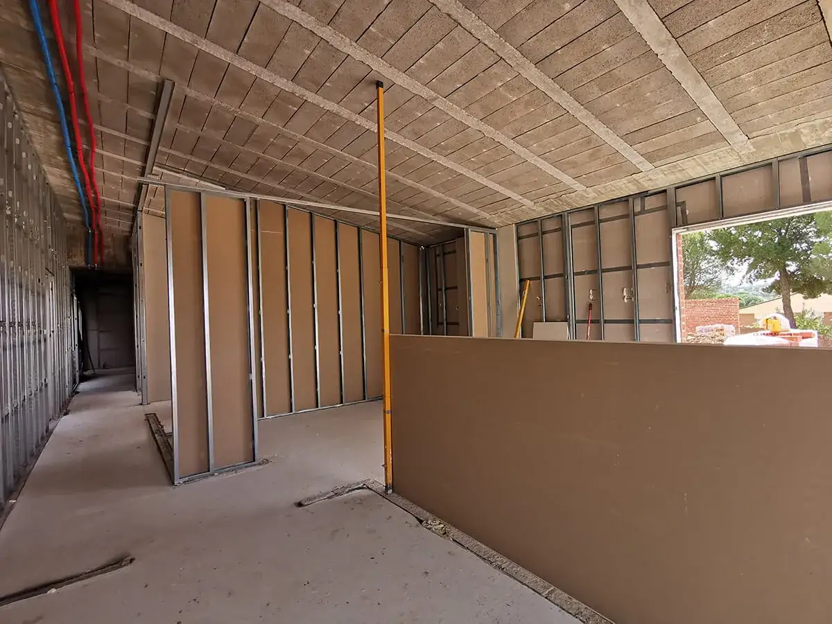 Interior de una casa en construcci&oacute;n, con estructuras met&aacute;licas y tabiques de cart&oacute;n yeso. Se aprecian tuber&iacute;as de agua y el techo de viguetas.