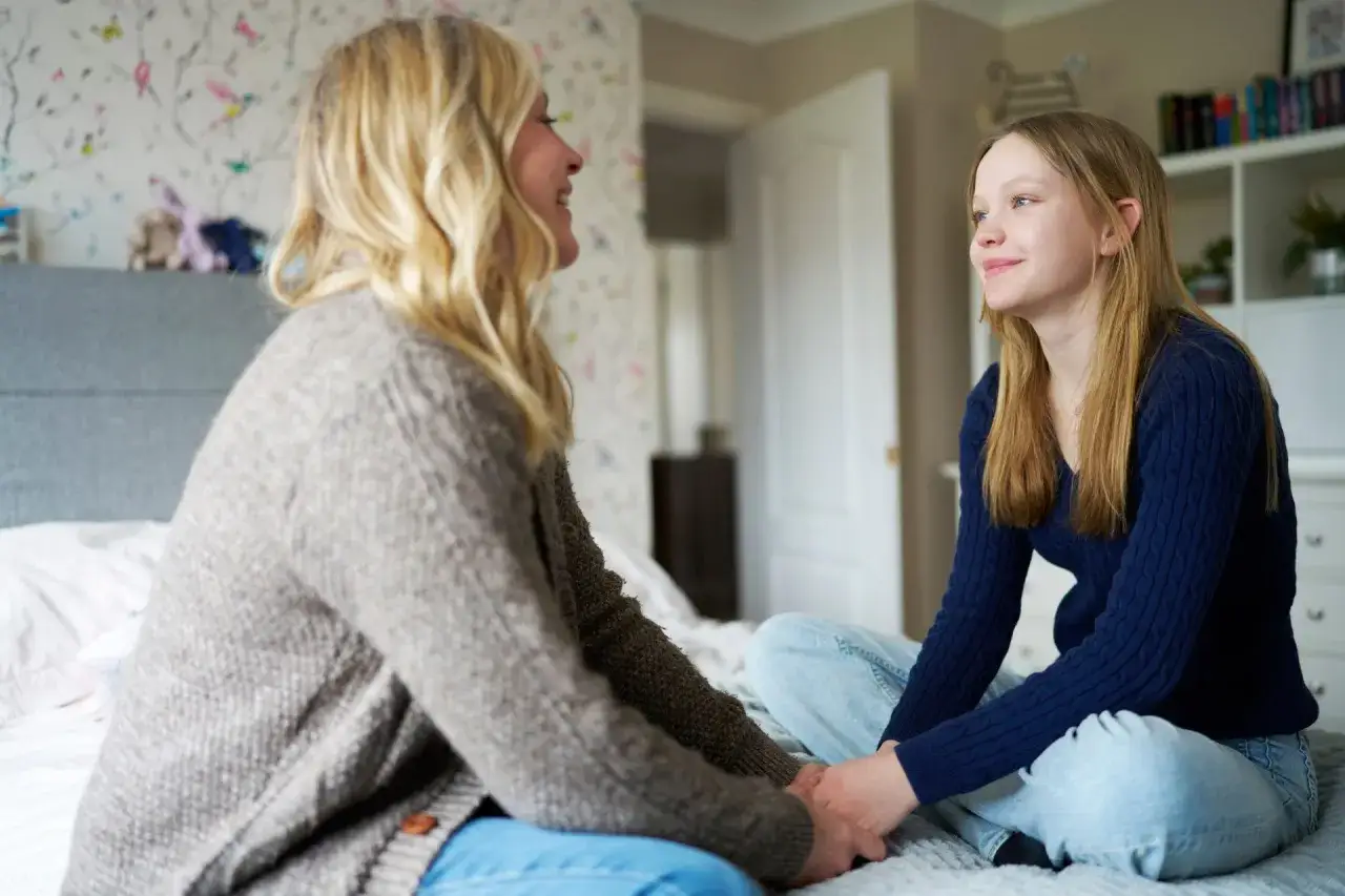 Madre e figlia si tengono per mano sul letto, un momento di ascolto e supporto per capire come aiutare un figlio depresso.