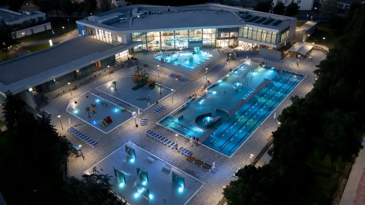 Nowoczesne łódź baseny termalne nocą, z podświetlanymi nieckami, zjeżdżalniami i leżakami.