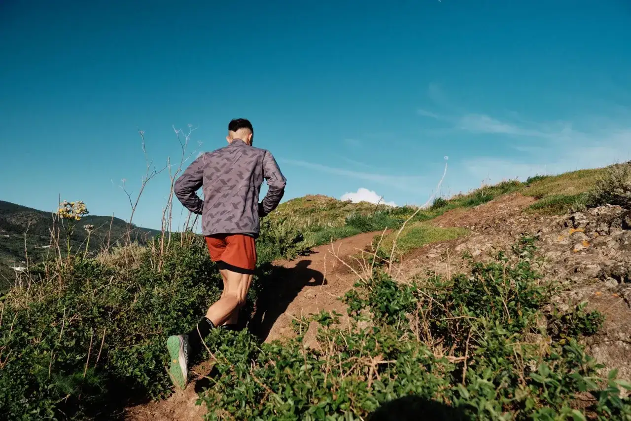 Un coureur s'élance sur un sentier escarpé, défiant un trail de 15 km sans entraînement. Le soleil brille sous un ciel bleu intense.