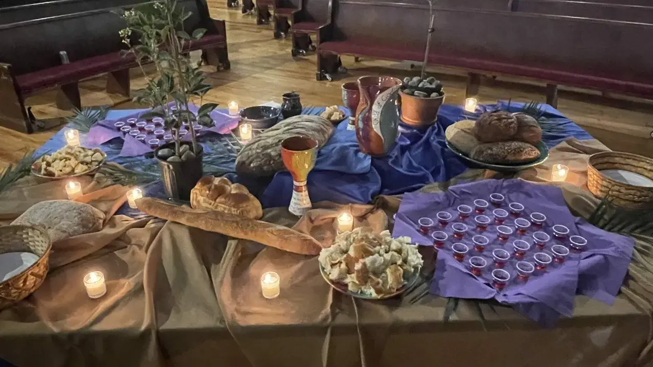 A table set for Eucharist, with bread and wine in small cups, ready for communion. Candles flicker, creating a solemn atmosphere.