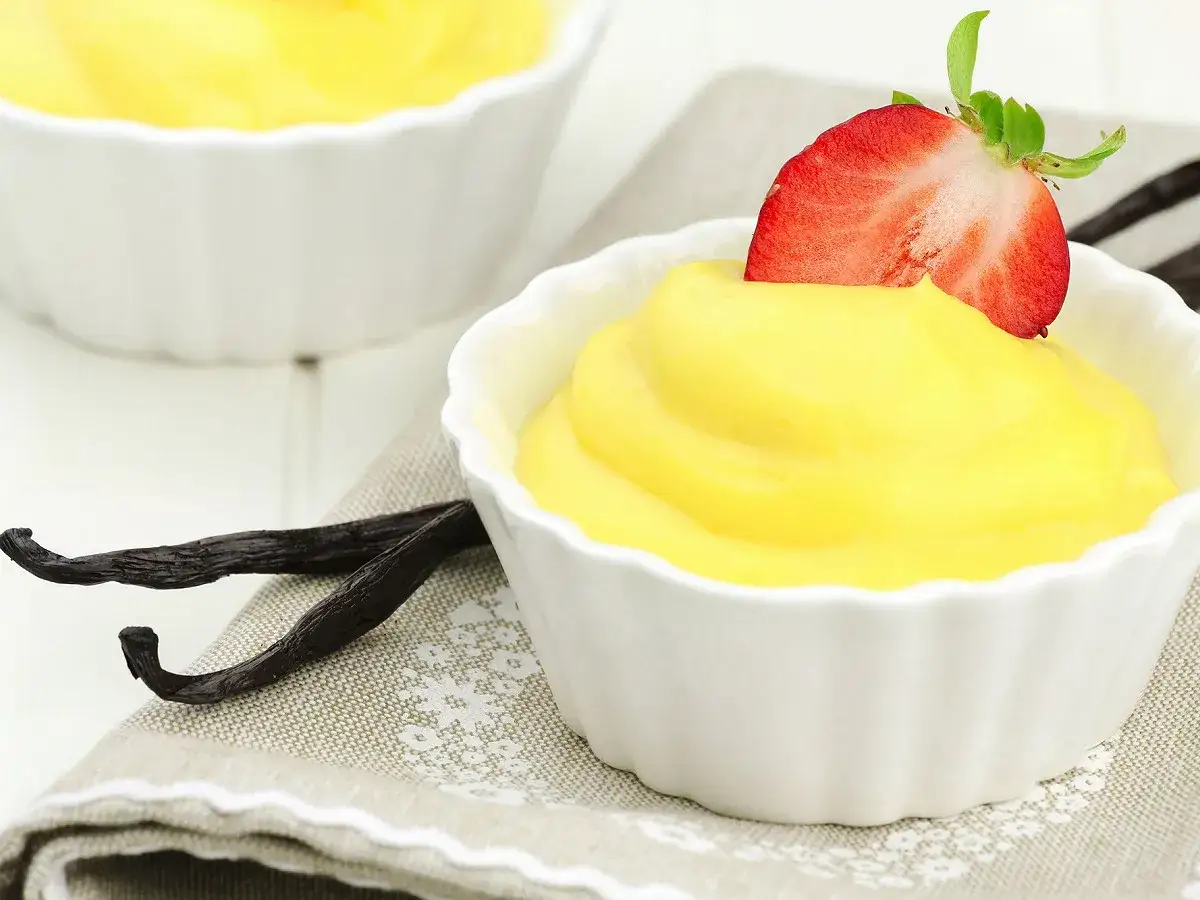 Crème mousseline onctueuse dans des ramequins blancs, garnie d'une fraise et accompagnée de gousses de vanille. Parfait pour savoir que faire avec de la crème mousseline.