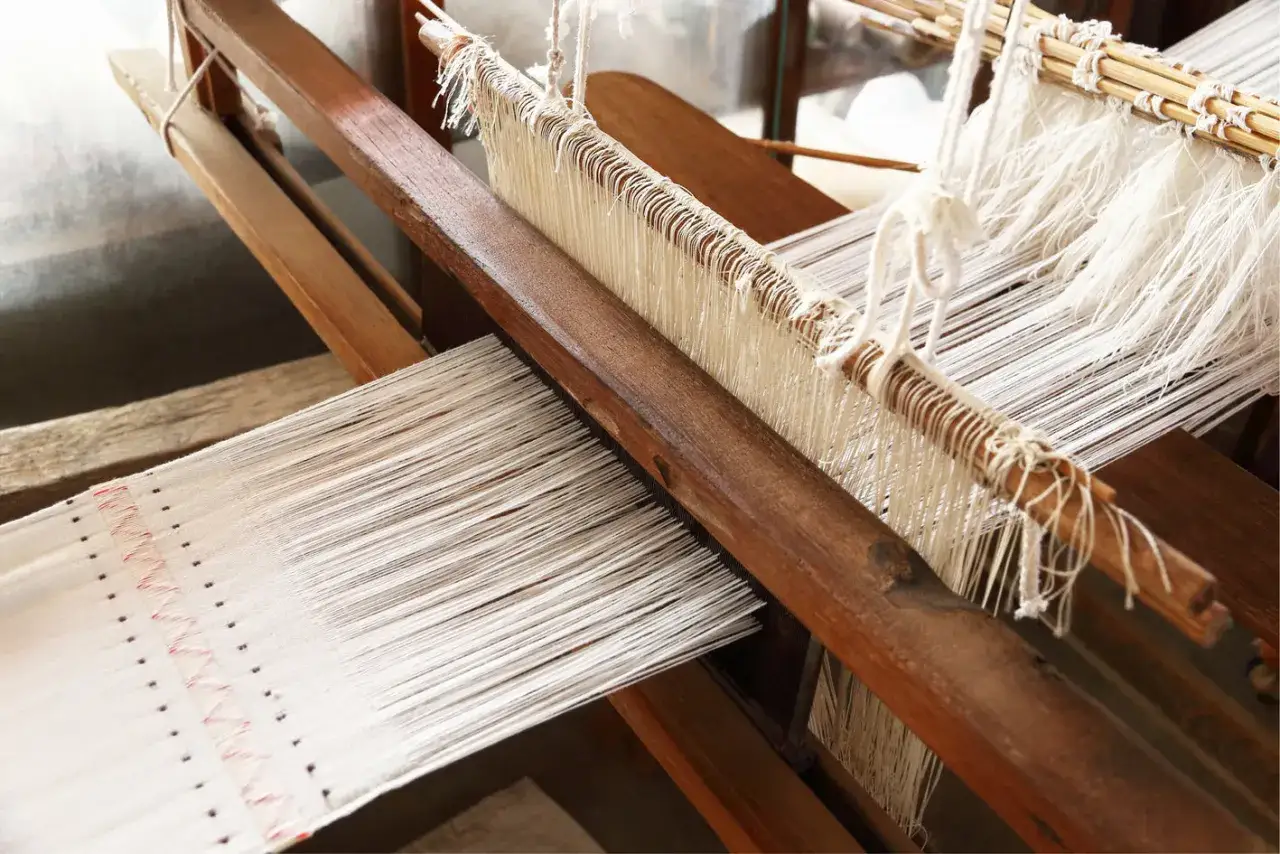 A close-up of a wooden loom, showcasing the intricate threads of handlooms of India being woven into fabric.
