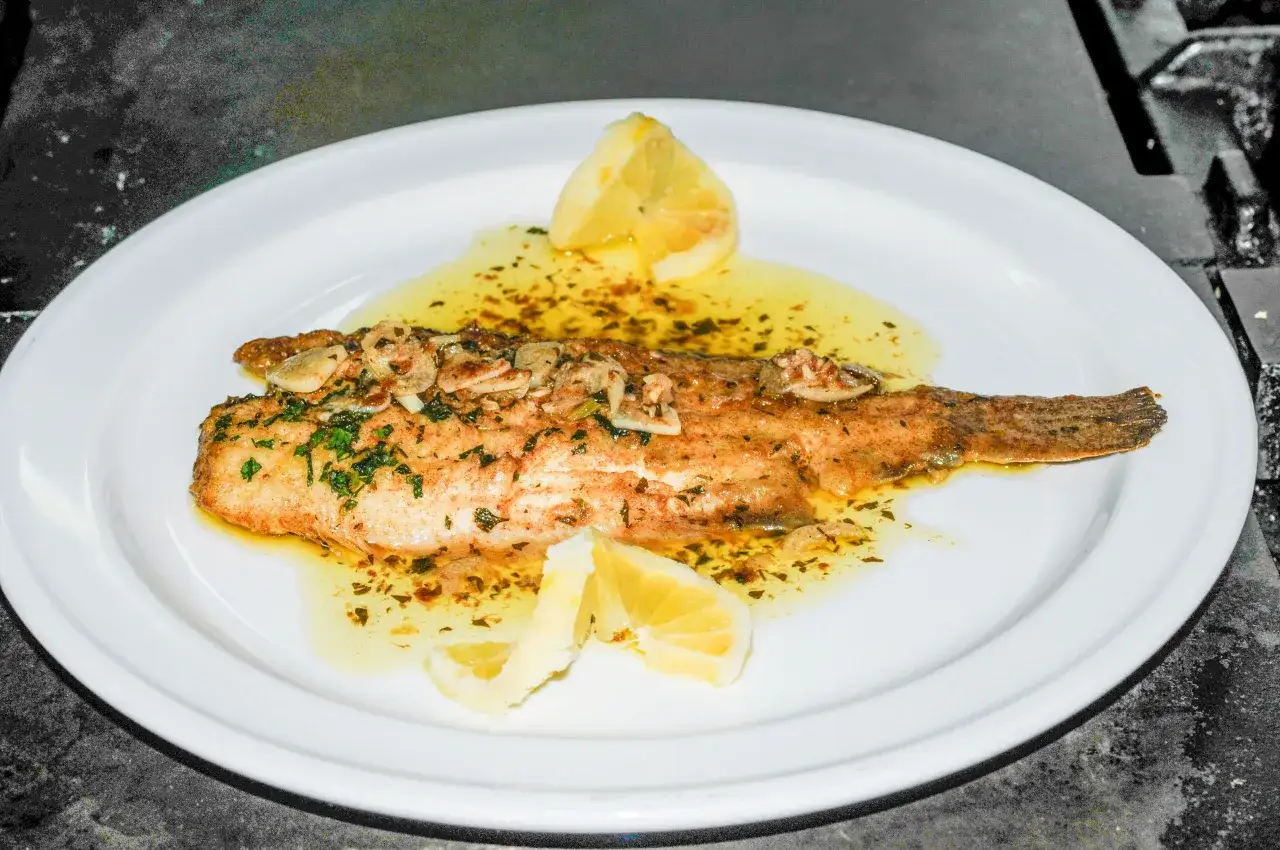 Delicioso lenguado a la meuni&egrave;re, ba&ntilde;ado en mantequilla dorada con ajo y perejil, adornado con gajos de lim&oacute;n fresco.