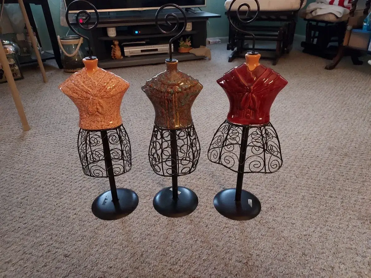 Tres maniqu&iacute;es peque&ntilde;os de cer&aacute;mica con faldas de alambre negro. Uno naranja, uno marr&oacute;n y uno rojo.