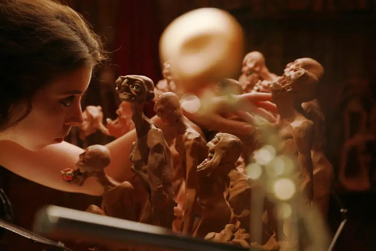 Una ragazza lavora a un'animazione stop motion, plasmando figure grottesche di argilla. Le sue mani muovono le creature in un mondo di fantasia.