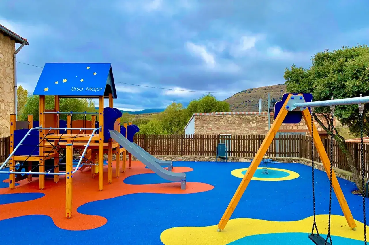 Una colorida zona de juegos para niños con columpios, tobogán y estructura de escalada bajo un cielo nublado.