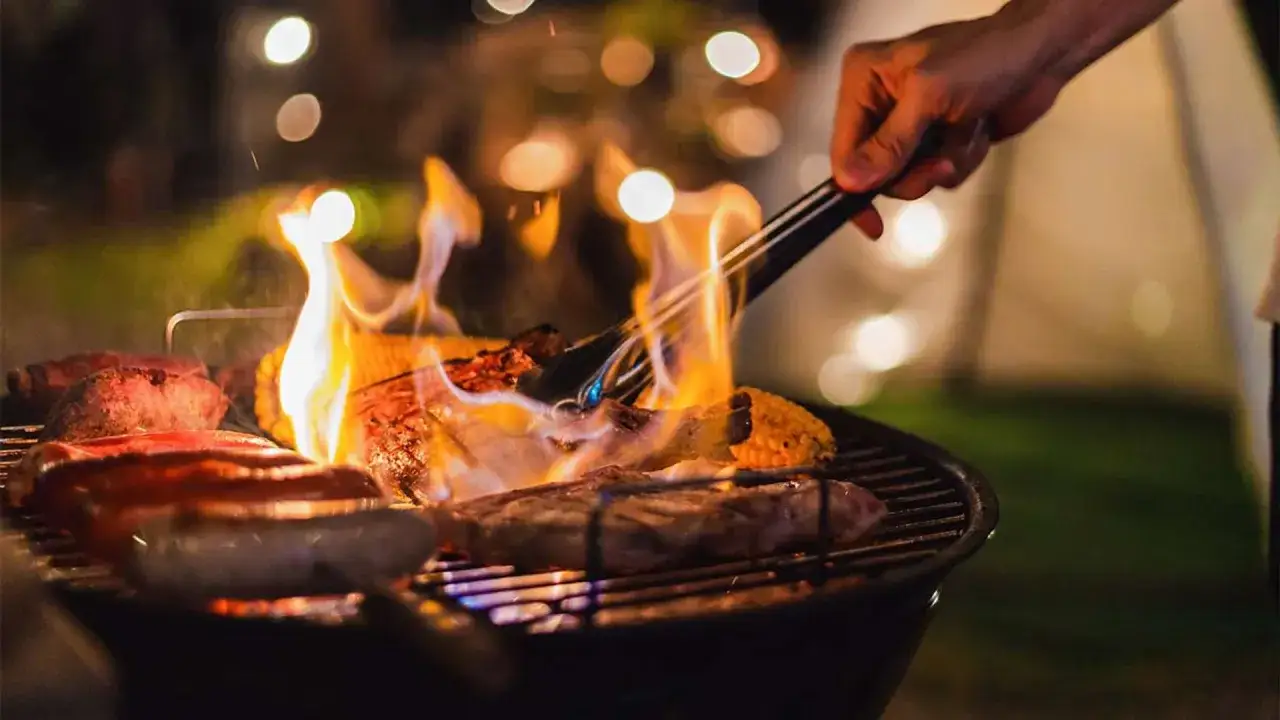 Carne y maíz asándose sobre brasas ardientes. La pregunta de cuánto tarda el carbón en hacer brasa se responde con esta escena de barbacoa nocturna.