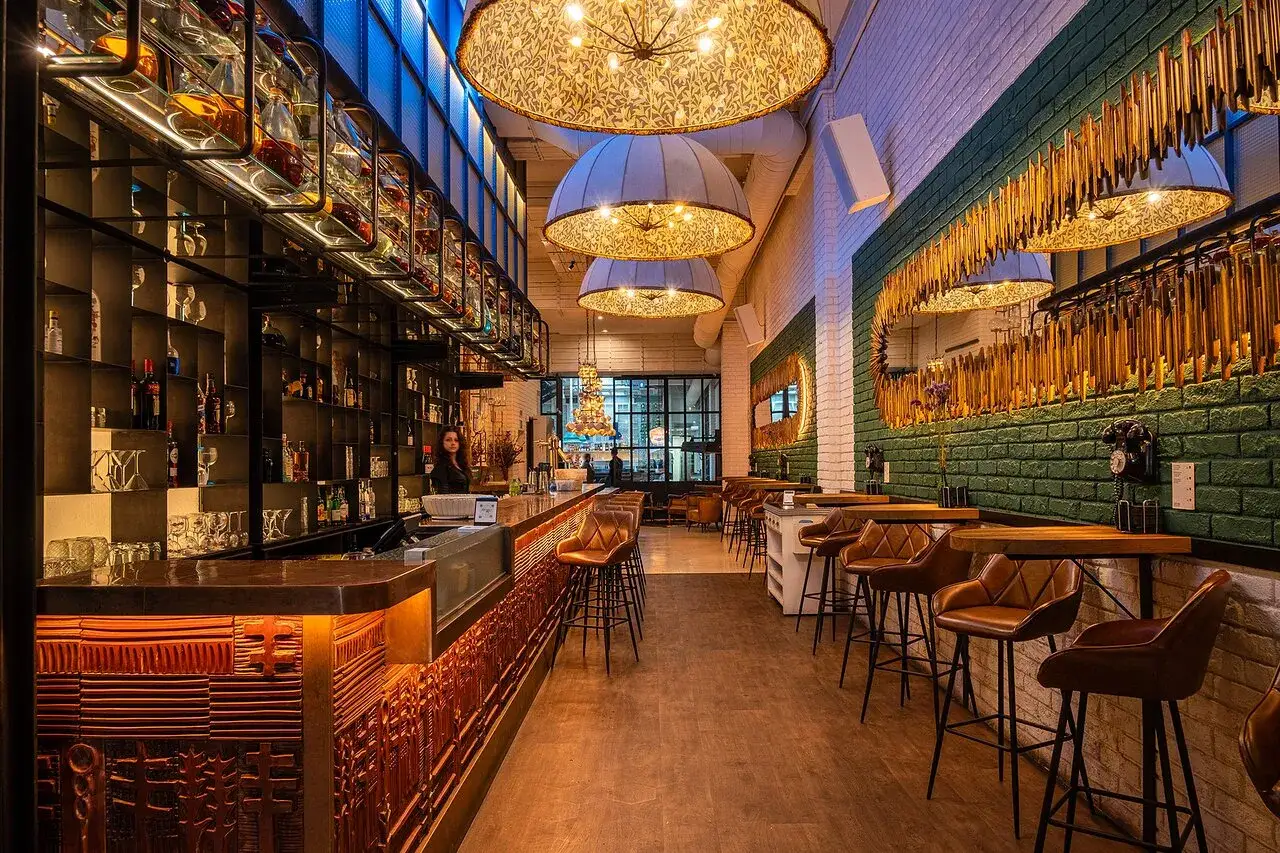 Interior de un moderno bistro bar con barra iluminada, estanter&iacute;as de licores, taburetes de cuero y decoraci&oacute;n chic.