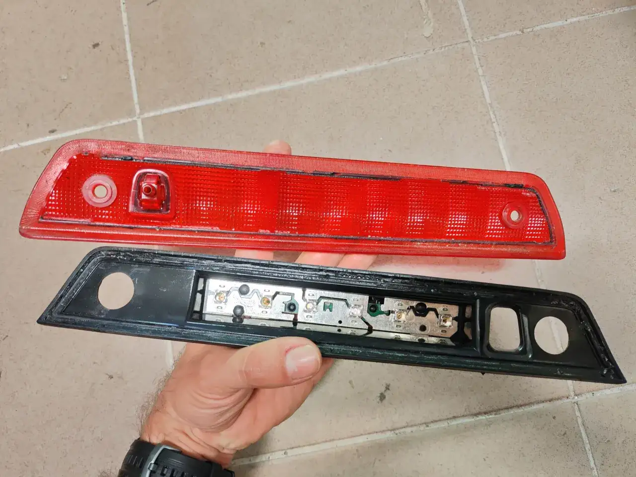Czerwona obudowa i czarna podstawa z elementami elektrycznymi, gotowe do montażu trzeciego światła stopu.