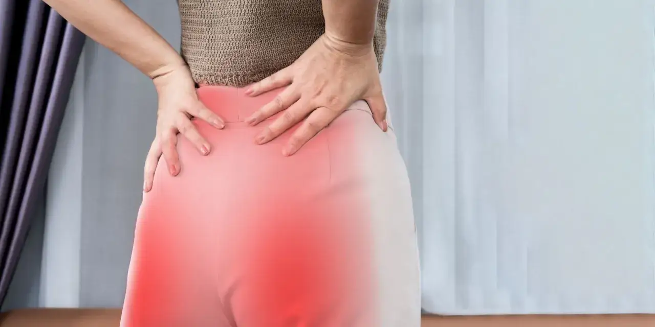 Kobieta trzyma się za bolące biodra i dolną część pleców, co sugeruje ból korzonków.