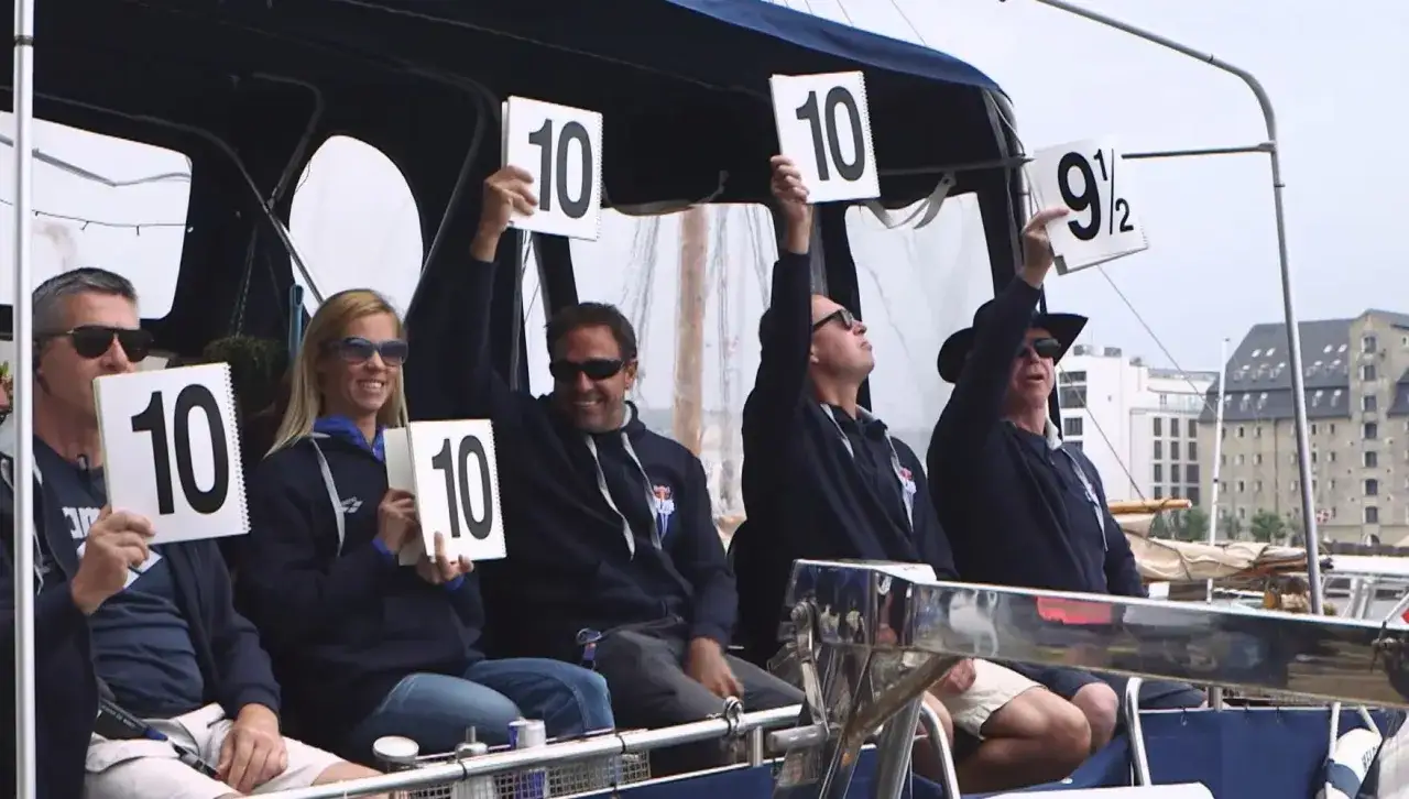 Judges on a boat hold up scorecards, with several showing a perfect 10, indicating a high diving score.
