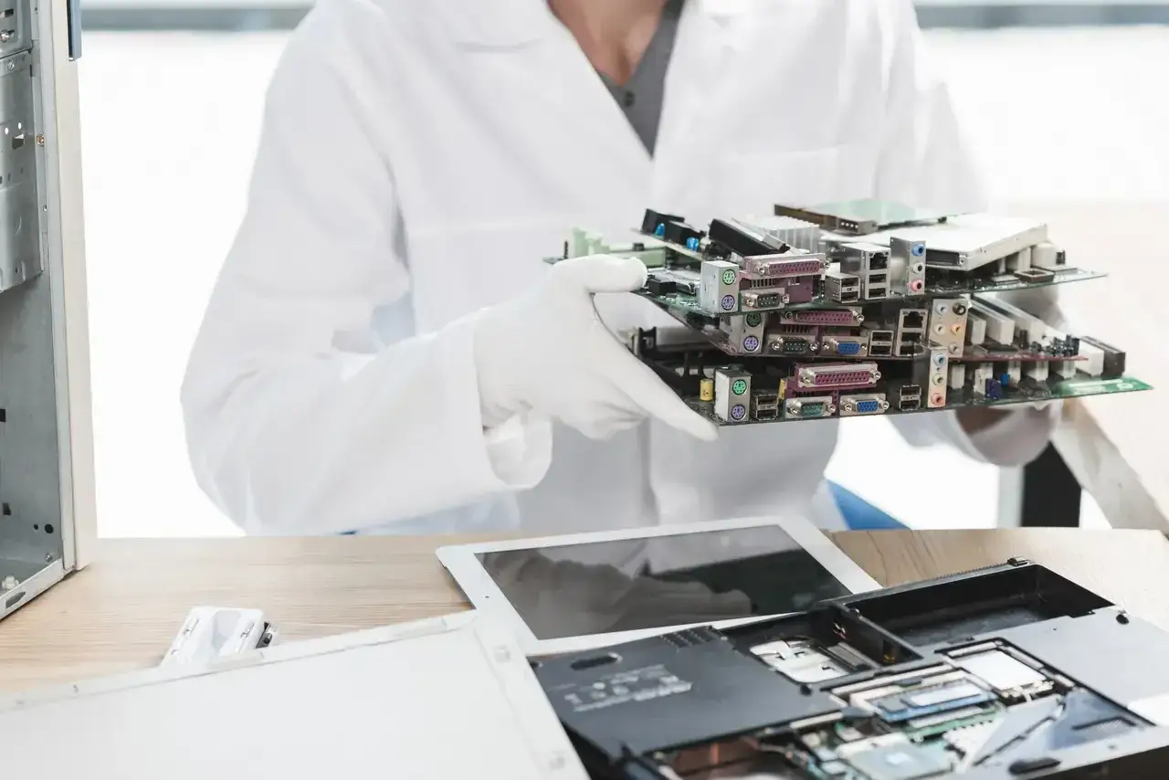 Osoba w białej rękawiczce trzyma stos płyt głównych. Zastanawiasz się, gdzie oddać stary laptop? To miejsce pomoże Ci w recyklingu.