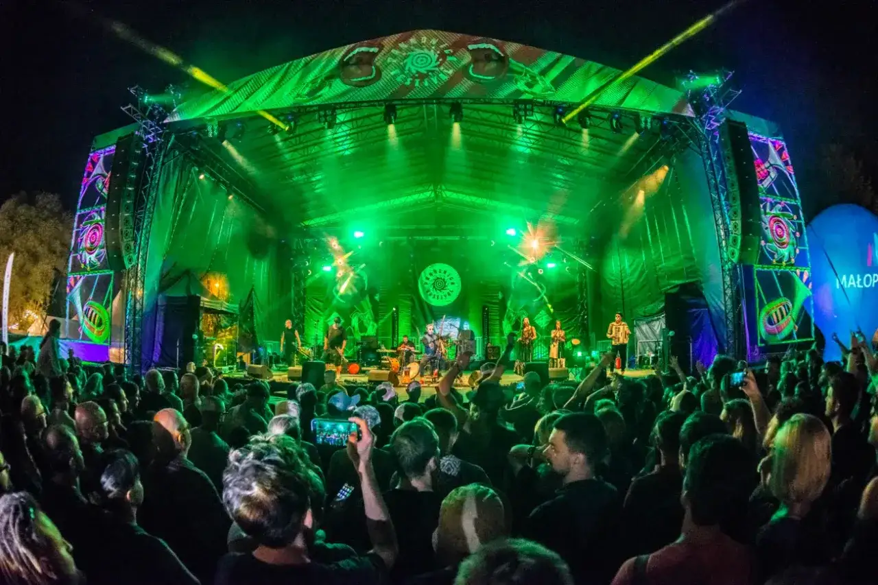 Koncert na festiwalu Pannonica. Tłum widz&oacute;w pod sceną oświetloną na zielono, zesp&oacute;ł grający muzykę.