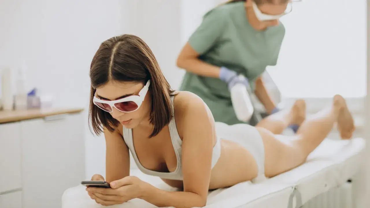 Kobieta na fotelu kosmetycznym, podczas depilacji laserowej, przegląda telefon. Zastanawiasz się, depilacja laserowa od ilu lat jest dostępna?
