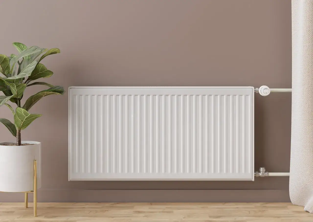 Radiador blanco moderno, parte de un sistema de calefacci&oacute;n por radiadores, junto a una planta y cortinas.